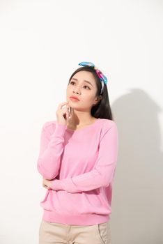 Portrait of a thoughtful young asian woman looking up at copy space with hand on her chin isolated over white background