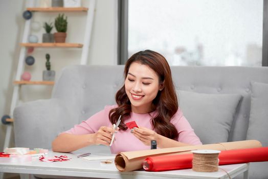 Smiling girl cutting valentine heart out of red paper with scissors in living room