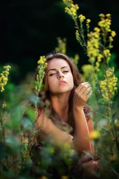 Soft portrait of a young woman sitting with a languid eyes among wildflowers