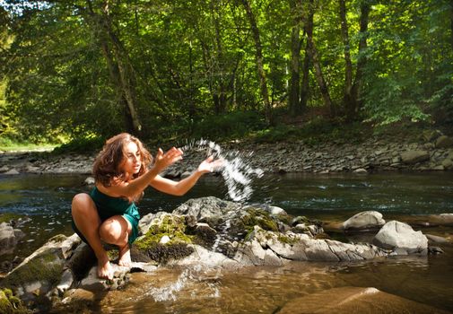 Young  woman playing with water near the forest river