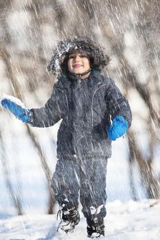 In the snowfall. Cute boy walk in the winter park in sunny day