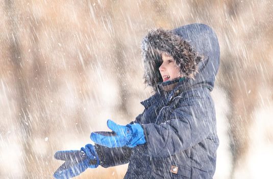 Snowfall. Cute boy in a winter jacket, playing with snowflakes