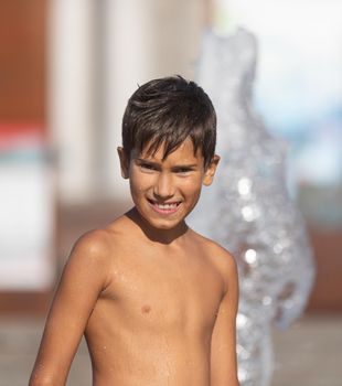 11 years old happy boy playing in a water fountain and enjoying the cool streams of water in a hot day. Hot summer.