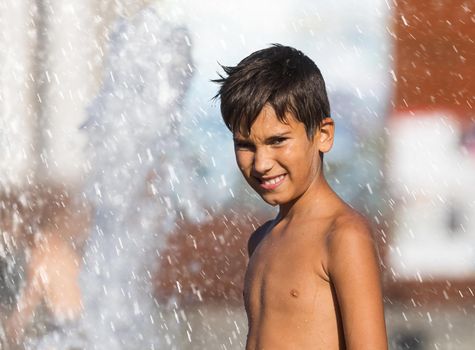 11 years old happy boy playing in a water fountain and enjoying the cool streams of water in a hot day. Hot summer.