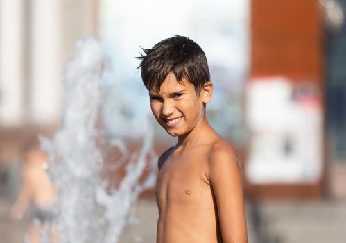 11 years old happy boy playing in a water fountain and enjoying the cool streams of water in a hot day. Hot summer.