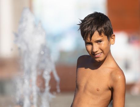 11 years old happy boy playing in a water fountain and enjoying the cool streams of water in a hot day. Hot summer.