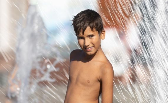 11 years old happy boy playing in a water fountain and enjoying the cool streams of water in a hot day. Hot summer.