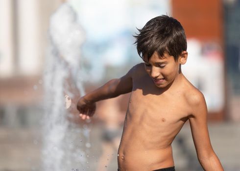 11 years old happy boy playing in a water fountain and enjoying the cool streams of water in a hot day. Hot summer.