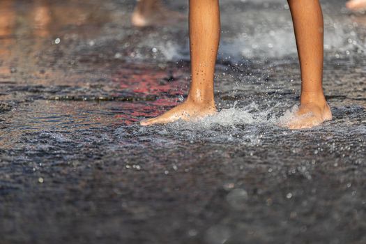 Happy children playing in a water fountain in a hot day. Close-up of children legs in a fountain