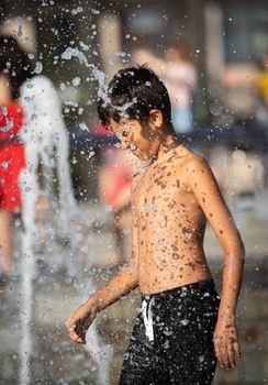 11 years old happy boy playing in a water fountain and enjoying the cool streams of water in a hot day. Hot summer.