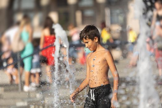 11 years old happy boy playing in a water fountain and enjoying the cool streams of water in a hot day. Hot summer.