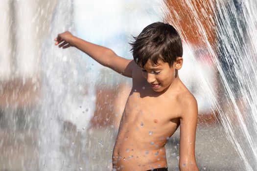 11 years old happy boy playing in a water fountain and enjoying the cool streams of water in a hot day. Hot summer.