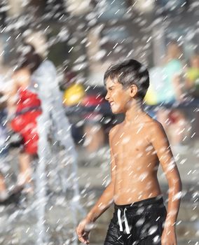 11 years old happy boy playing in a water fountain and enjoying the cool streams of water in a hot day. Hot summer.