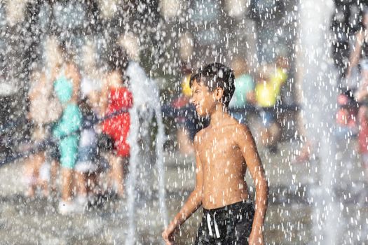 11 years old happy boy playing in a water fountain and enjoying the cool streams of water in a hot day. Hot summer.