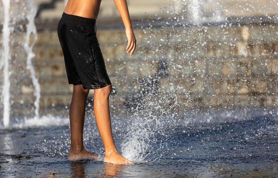 Happy children playing in a water fountain in a hot day. Close-up of children legs in a fountain