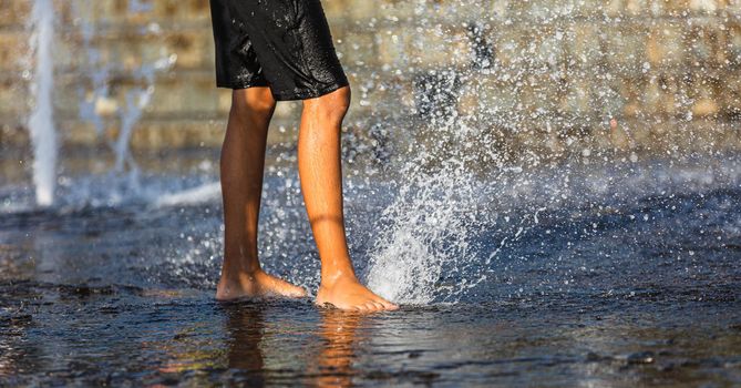 Happy children playing in a water fountain in a hot day. Close-up of children legs in a fountain