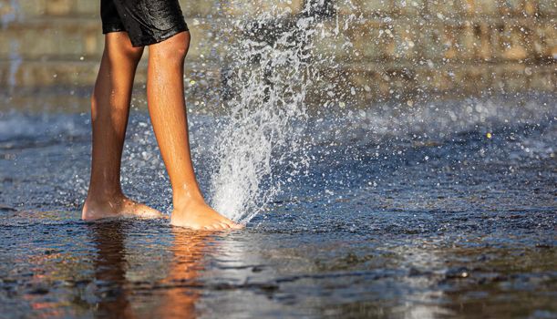 Happy children playing in a water fountain in a hot day. Close-up of children legs in a fountain