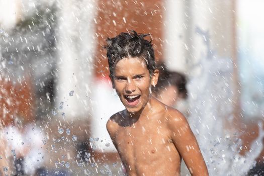 11 years old happy boy playing in a water fountain and enjoying the cool streams of water in a hot day. Hot summer.