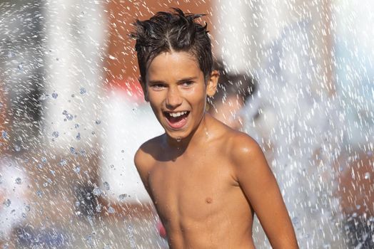 11 years old happy boy playing in a water fountain and enjoying the cool streams of water in a hot day. Hot summer.