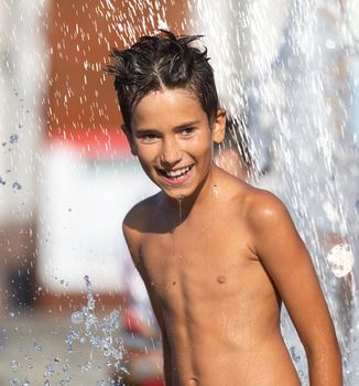 11 years old happy boy playing in a water fountain and enjoying the cool streams of water in a hot day. Hot summer.