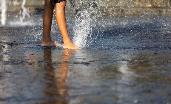 Happy children playing in a water fountain in a hot day. Close-up of children legs in a fountain