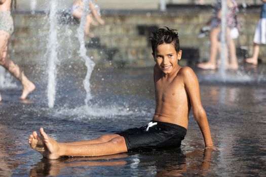 11 years old happy boy playing in a water fountain and enjoying the cool streams of water in a hot day. Hot summer.