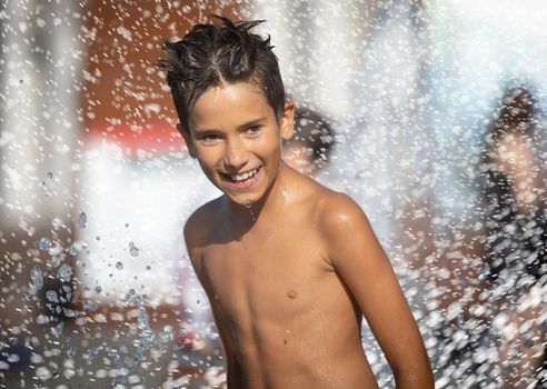 11 years old happy boy playing in a water fountain and enjoying the cool streams of water in a hot day. Hot summer.