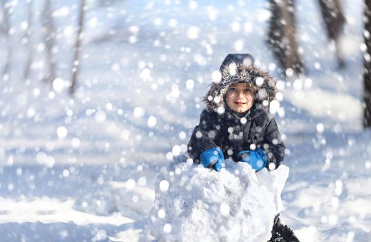 Cute boy playing with snow in the winter park  during a snowfall on a winter day