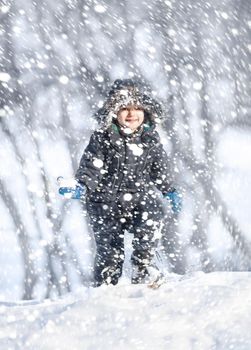 Cute boy playing with snow in the winter park  during a snowfall on a winter day