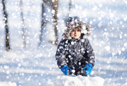 Cute boy playing with snow in the winter park  during a snowfall on a winter day