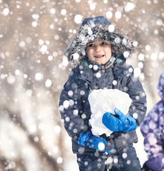 Cute boy playing with snow in the winter park  during a snowfall on a winter day