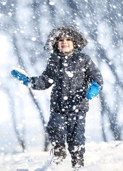 Cute boy playing with snow in the winter park  during a snowfall on a winter day