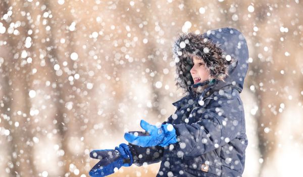 Cute boy playing with snow in the winter park  during a snowfall on a winter day