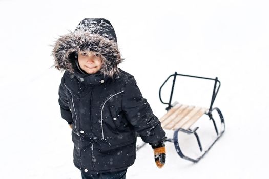Winter photo of cute young boy in winter suit pulling snow sledges through the snow