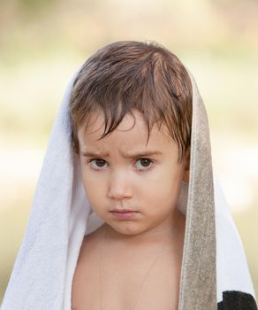Portrait of a three year old boy with a serious expression on his face and a towel on his head