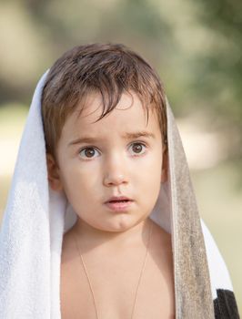 Portrait of a three year old boy with a serious expression on his face and a towel on his head