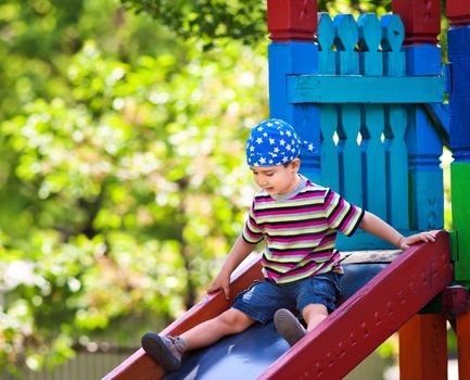 Cute boy in bandana playing on slide