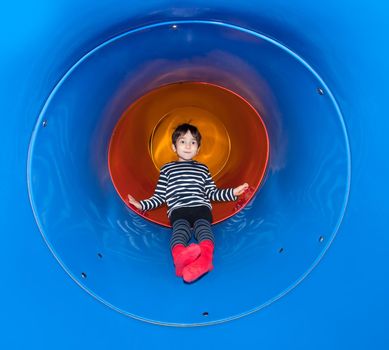 Joyful kid sliding in tube slide on playground