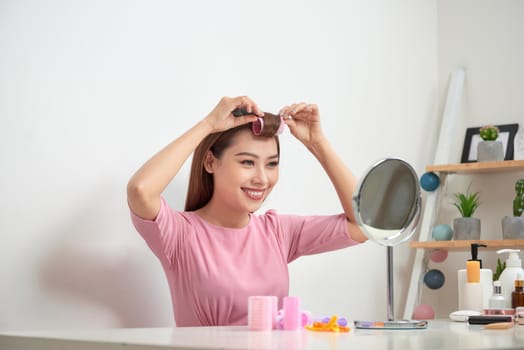 Beautiful woman with curlers smiling into mirror, enjoying her look, beauty
