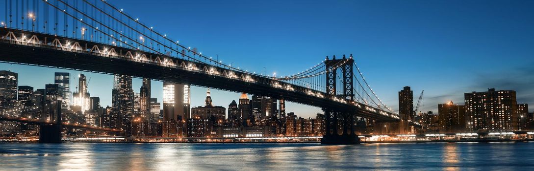 Manhattan Skyline and Manhattan Bridge At Night. Manhattan Bridge is a suspension bridge that crosses the East River in New York City. 