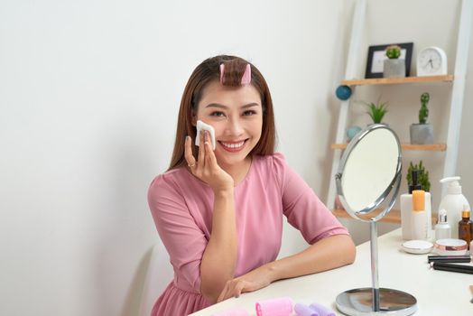 Cosmetic beauty procedures and makeover concept. Woman in hair curlers beautiful young woman using cotton pads at home