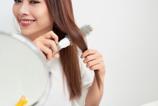 Getting rid of tangles. Beautiful young woman looking at her reflection in mirrorand brushing her long hair while sitting at the dressing table