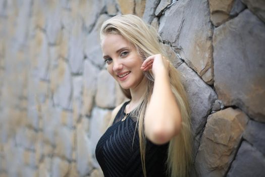 Portrait of Beautiful blonde hair girl on black dress against stone wall as fashion portrait outdoor.