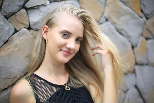 Portrait of Beautiful blonde hair girl on black dress against stone wall as fashion portrait outdoor.