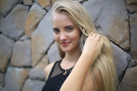 Portrait of Beautiful blonde hair girl on black dress against stone wall as fashion portrait outdoor.