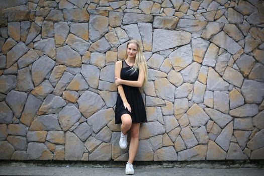 Portrait of Beautiful blonde hair girl on black dress against stone wall as fashion portrait outdoor.