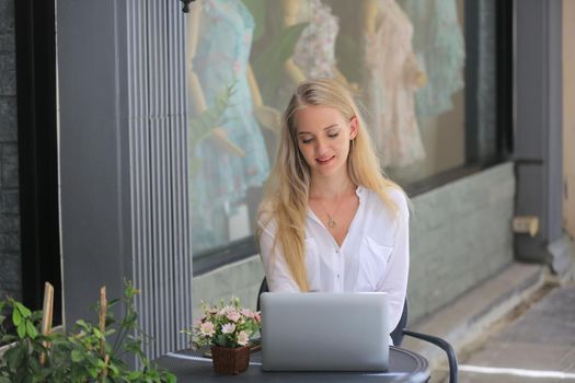 Beautiful blonde hair girl sitting with laptop in front of retails shop,Small business owner concept