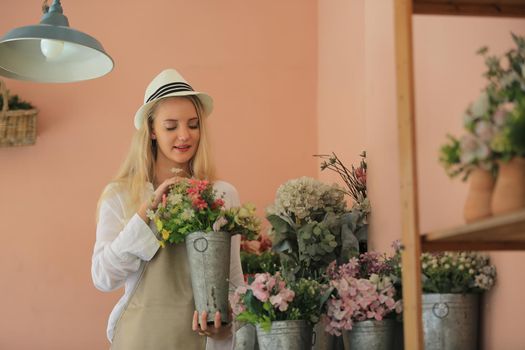 Beautiful blonde hair girl standing with confidence in front of flower in open retails flora shop. Small business owner concept.