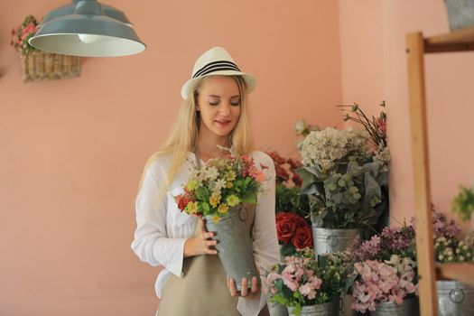 Beautiful blonde hair girl standing with confidence in front of flower in open retails flora shop. Small business owner concept.