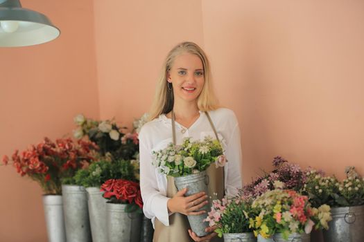 Beautiful blonde hair girl standing with confidence in front of flower in open retails flora shop. Small business owner concept.